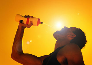 thirsty man drinking from water bottle in front of orange sunset